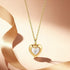 Gold heart-shaped pendant necklace with a white stone on a soft pink background